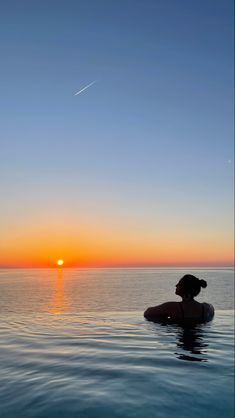 a woman sitting on top of a surfboard in the middle of water at sunset