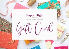 paper high gift card surrounded by other wrapping materials and crafting supplies on a white surface