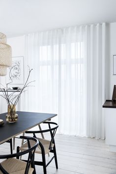 a dining room table with chairs and vases on it, in front of white curtains