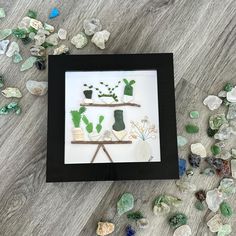 some rocks and plants are sitting on the floor next to a black frame with glass shards scattered around it