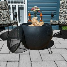 a fire pit sitting on top of a patio next to two chairs and a table