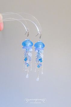 These earrings feature delicate blue glass beads and silver chains, perfectly mimicking the ethereal beauty of jellyfish floating in the ocean. The cascading chains and shimmering beads create a mesmerizing effect with every movement, making these earrings a captivating accessory for any outfit. Ideal for ocean lovers and those who adore statement jewelry. Perfect for beach outings, summer festivals, or as a thoughtful gift for someone who loves the sea. - Width: 3/4" | 1.9cm - Length: 3" | 7.6c Blue Dangle Earrings With Ocean-inspired Style, Ocean-inspired Blue Dangle Earrings, Jelly Fish Earrings, Blue Ocean-inspired Dangle Jewelry, Melanie Concert, Floating In The Ocean, Ocean Accessories, Jellyfish Jewelry, Water Earrings