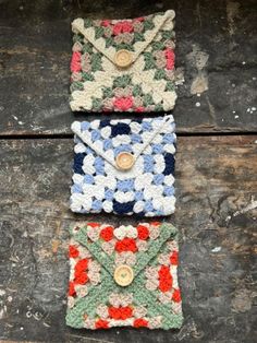 three crocheted envelopes sitting next to each other on a wooden surface with buttons