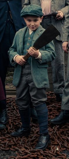 a little boy in a suit and hat holding a knife while standing next to other people