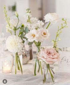 three vases filled with flowers sitting on top of a white tablecloth covered table