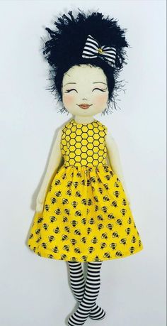 a doll with black hair wearing a yellow dress and striped socks is standing in front of a white wall