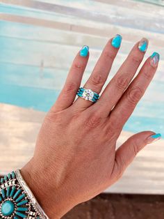 a woman's hand with blue and white nail polish holding up her turquoise ring