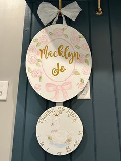 two plates hanging on the wall with names and numbers painted on them, one has a pink bow