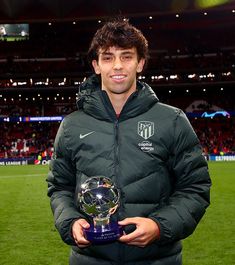 a man holding a soccer ball and trophy in front of a stadium filled with people