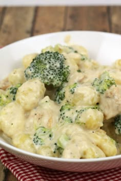 a white bowl filled with broccoli covered in cheese and sauce on top of a red checkered cloth