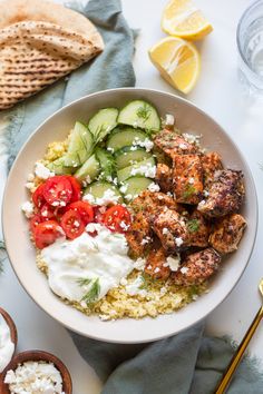 a white bowl filled with chicken, cucumber and tomatoes next to pita bread