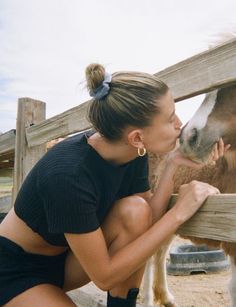 a woman is petting a horse in an enclosed area with wood fence and wooden posts