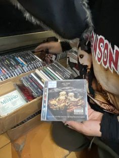 a person holding a cd in front of a shelf full of dvds and cds on the floor