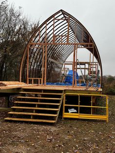 a wooden structure sitting in the middle of a field next to some stairs and trees