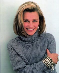 a woman with her arms crossed posing for a photo in front of a white wall