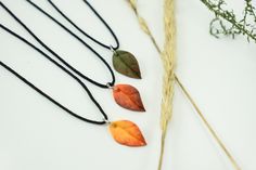 three necklaces with leaves on them sitting next to some dried grass and plants in the background