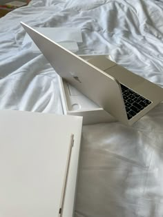 an open laptop computer sitting on top of a white sheet covered bed next to a box