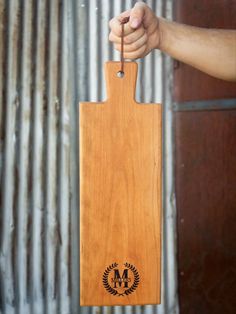 a person holding a wooden cutting board with an emblem on the front and back side