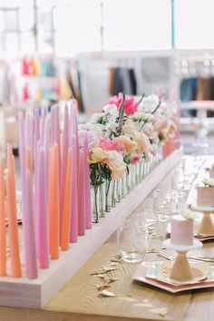 there are many candles on the table with flowers in vases next to each other