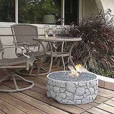 a fire pit sitting on top of a wooden deck next to chairs and table with plants