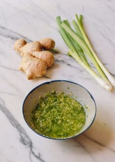 a bowl filled with green liquid next to some celery and ginger stalks on a marble surface