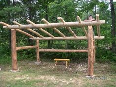 a man sitting on top of a wooden bench under a pergolated structure in the woods