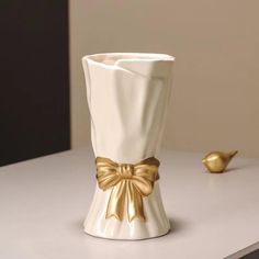 a white vase with a gold bow on the side sitting on top of a table