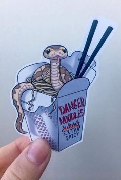 a hand holding up a sticker with an image of a snake eating noodles