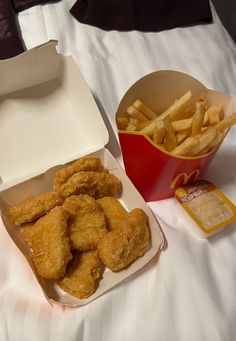 chicken nuggets and french fries are sitting on a bed next to a box of macaroni and cheese