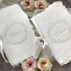 two white napkins with ribbons and flowers on a glass plate next to each other