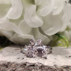 an engagement ring sitting on top of a stone slab next to white flowers and peonies