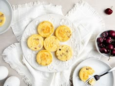 an assortment of desserts on plates with cherries next to them and bowls of cherries