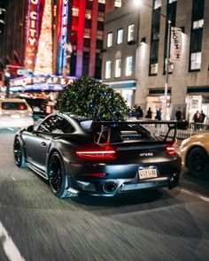 a black sports car driving down the street in front of a christmas tree on top of it