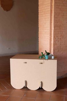 a white cabinet sitting on top of a tile floor next to a brick wall and potted plant