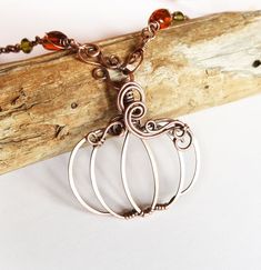 a necklace with two metal pumpkins hanging from it's sides on a piece of wood