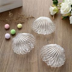 three glass seashells sitting on top of a wooden table next to white flowers