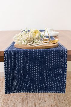 a blue table runner with white flowers on it and a wooden tray in the middle