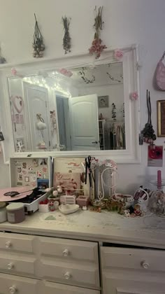 a white dresser topped with lots of clutter next to a wall mounted vanity mirror