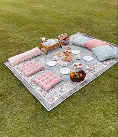 an outdoor picnic is set up on the grass with pink cushions and plates in front of it