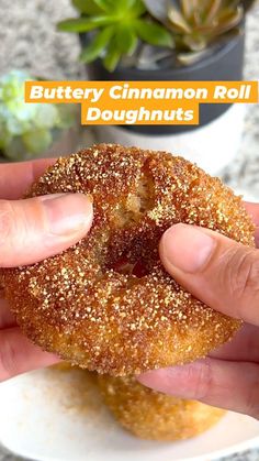 a person holding a sugared doughnut in their hand with the words buttery cinnamon roll doughnuts above it