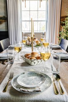 a table set with plates, silverware and candlesticks in front of a window