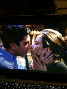 a man and woman kissing each other in front of a laptop screen with the image on it