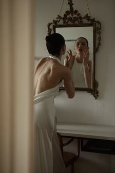 a woman in a white dress is looking at her reflection in the mirror while brushing her teeth