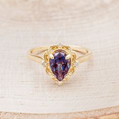 a gold ring with a heart shaped purple stone surrounded by small white diamonds on a piece of wood