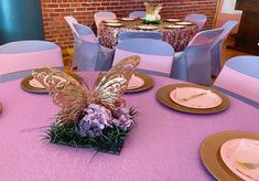 the table is set with pink and gold plates, napkins, and butterfly centerpieces