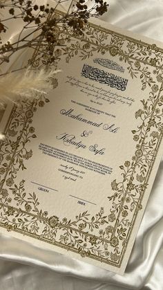 an ornate wedding card on a white satin sheet with feathers and flowers in the background