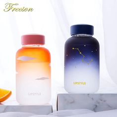 two bottles sitting next to each other on top of a white table with an orange slice