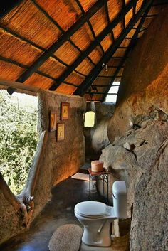 a bathroom with stone walls and flooring next to a large rock wall in front of the toilet