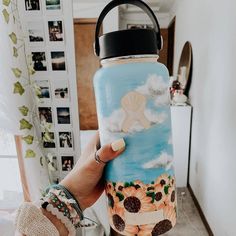 a person holding up a water bottle with sunflowers painted on the front and side