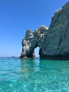 the water is crystal blue and there are people swimming in it near some large rocks